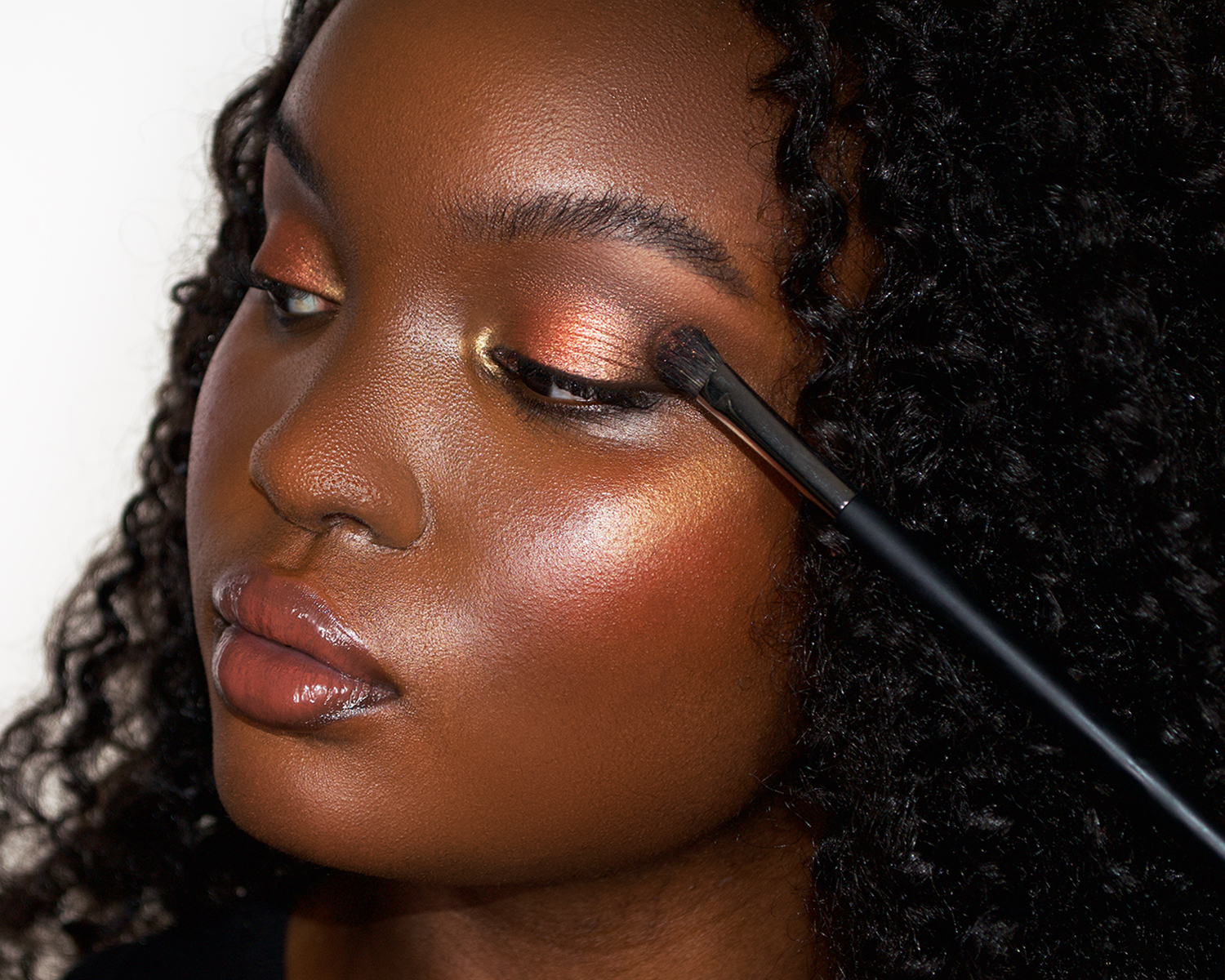 Close up of woman's face looking off to the side holding an eyeshadow brush to corner of her eye