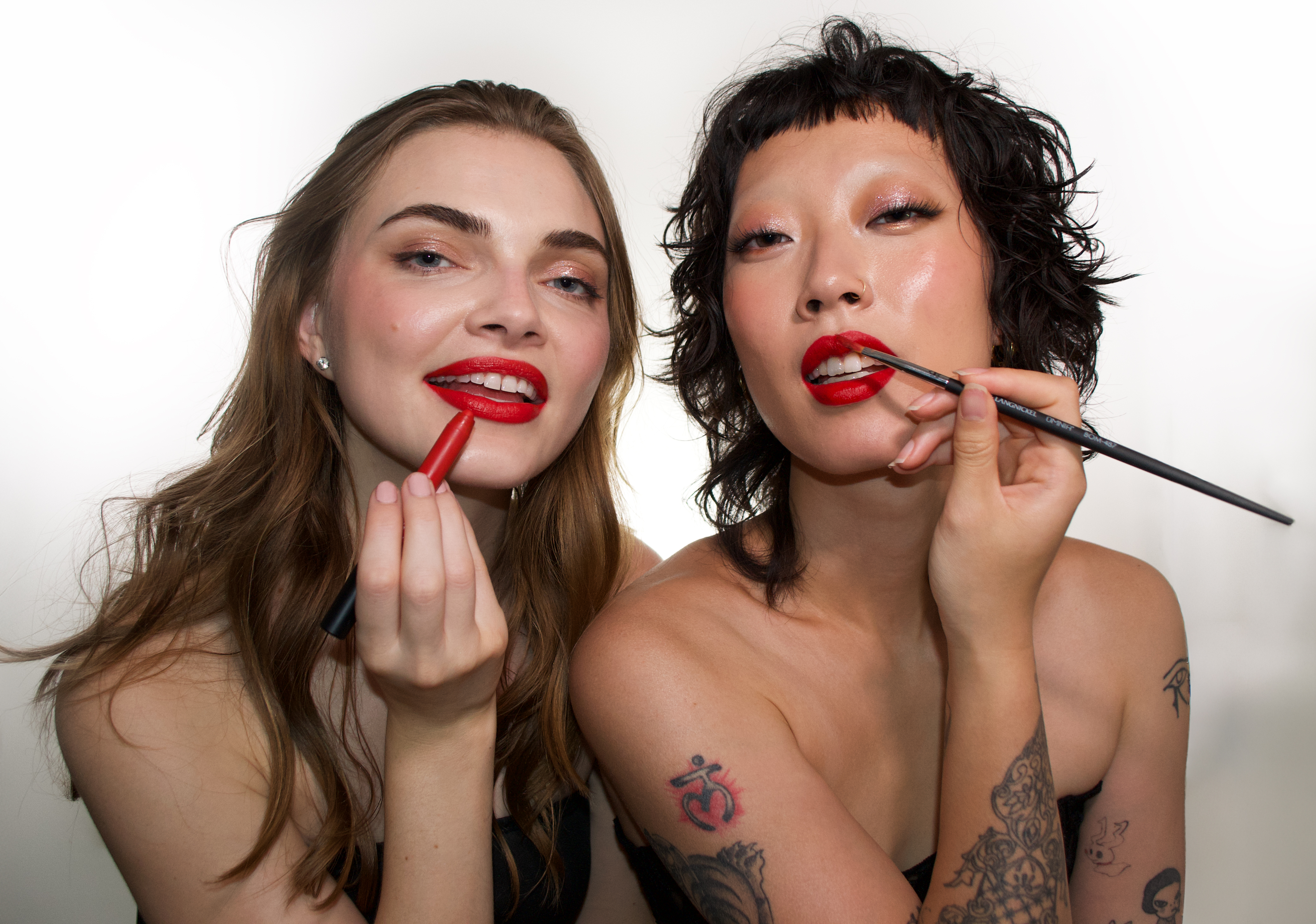 two women smiling and applying red lipliner